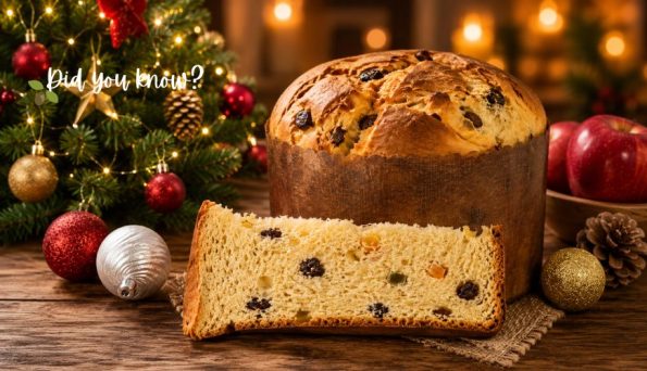 Panettone loaf with a slice cut and raisins on a wooden table, surrounded by Christmas tree ornaments and warm lights in a holiday setting.