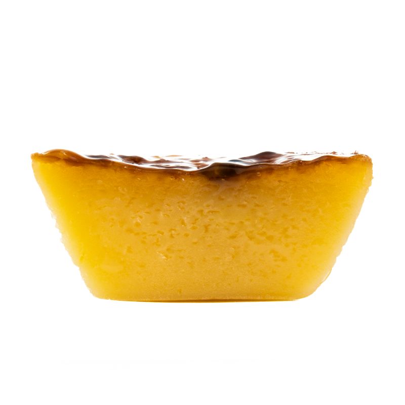 Queijada de Maracuja - Delícias Slice of yellow cheesecake with caramel glaze on top, set against a white background, facing left