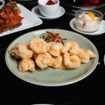 Golden fried shrimp tempura arranged on a green plate with a small vegetable garnish in the center.