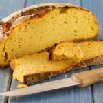 Rustic loaf of bread partially sliced on a blue wooden table with a bread knife nearby.