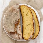 Rustic loaf of bread on a white plate with two thick slices showing a golden crust and soft crumb.