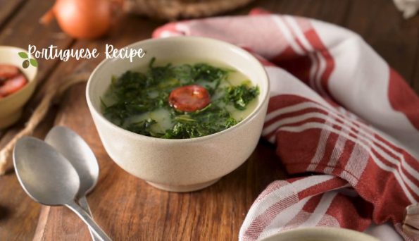 Bowl of Portuguese soup with greens and a cherry tomato on a wooden table, beside a red-striped cloth; ‘Portuguese Recipe’ logo visible in the corner.