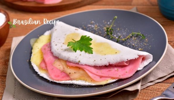 Folded ham-and-cheese crepe on a blue plate, garnished with parsley and herbs; Brazilian Recipe watermark in the corner.