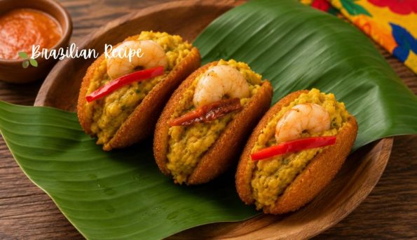Three shrimp-stuffed croquettes nestled on a green banana leaf on a wooden plate, with a Brazilian Recipe watermark in the corner.