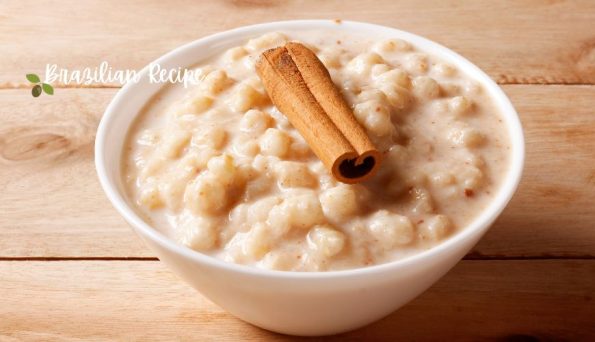 Creamy banana pudding in a white bowl with a cinnamon stick on a wooden table; Brazilian Recipe watermark
