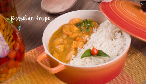 Shrimp curry served over white rice in an orange pot, garnished with a green leaf and red pepper.