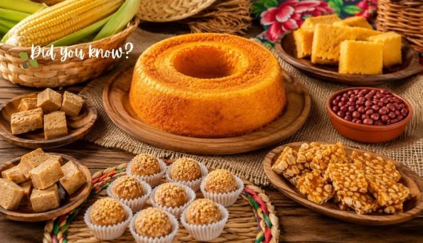 A rustic dessert table with a large ring cake surrounded by corn, cookies, sesame balls, and bite-sized treats on wooden boards.