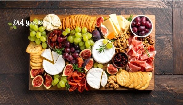 Charcuterie board with brie, grapes, figs, nuts, crackers and cured meat on a dark wooden table.