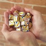 Two hands cupping a handful of small foil-wrapped candies with colorful wrappers and stars on the wrappers.