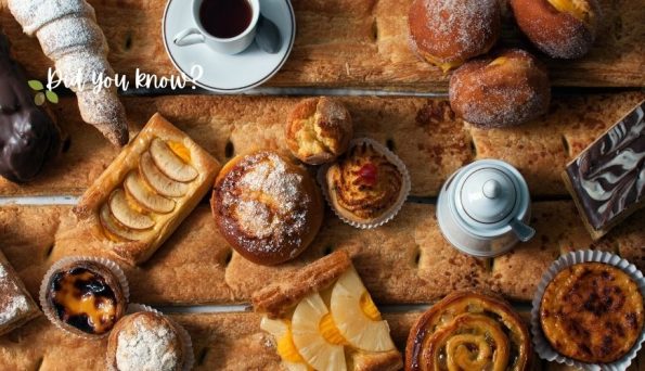 Assorted pastries on a rustic wooden baking sheet, including croissants, tarts, muffins, danishes, and a cup of coffee.