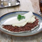 Pulled beef sandwich with mayonnaise on a folded white flatbread, garnished with a parsley leaf on a ceramic plate.