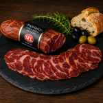 ChatGPT Image May 21 2026 12_14_28 PM - Delícias Sliced cured pork sausage arranged in front of a whole salami on a slate board, with bread, olives, and rosemary in the background