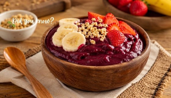 Wooden bowl of berry smoothie topped with banana slices, strawberries, and granola on a wooden table.