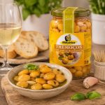 Platter of marinated tremoços (lupini beans) in oil with basil, beside a jar labeled 'Tremoços' and bread slices in the background.