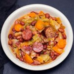 Hearty bean and sausage stew with carrots and cabbage in a light bowl, a comforting rustic dish.